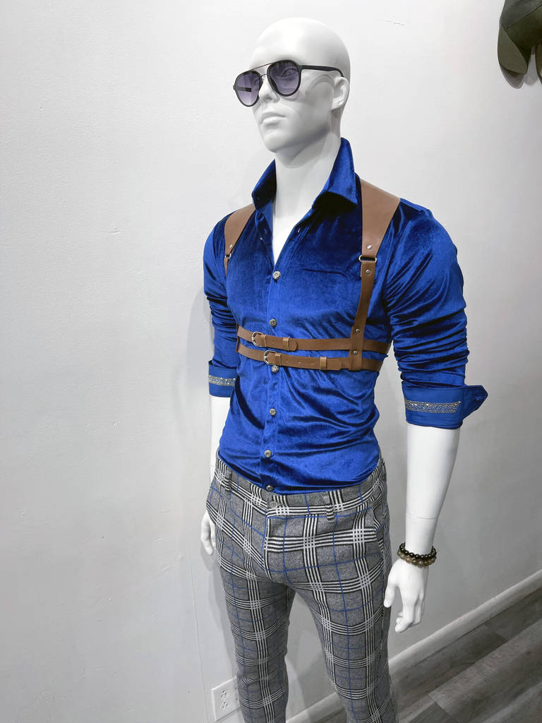 a white mannequin wear dark, gradient tint sunglasses, a royal blue, button down, long sleeve velvet shirt, a camel brown leather waist harness over the shirt, and light grey pants with a white, black and royal blue plaid pattern.