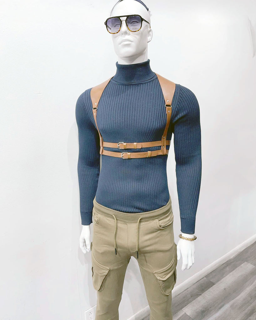 A white mannequin wearing sunglasses, a blue turtleneck sweater, a brown leather waist harness, and tan cargo joggers.