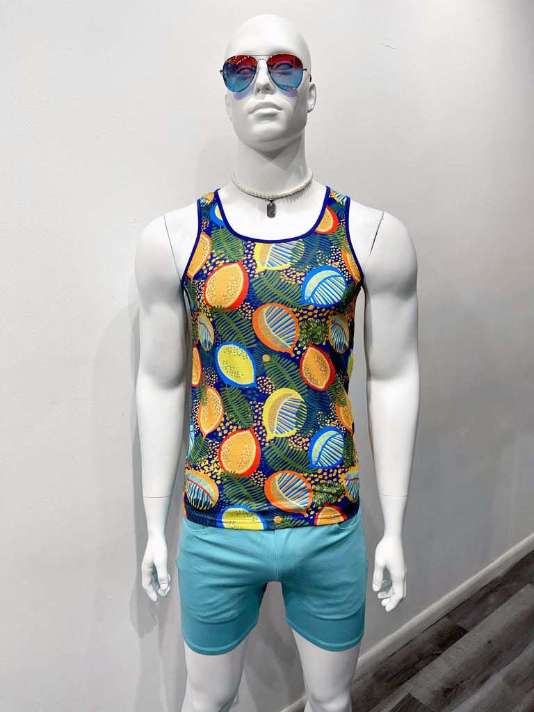 A mannequin in blue mirrored sunglasses, a thin gold chain with a gold dog tag, a tank top with a bright multicolor fruit pattern of yellow, green, orange, and red, with teal shorts.