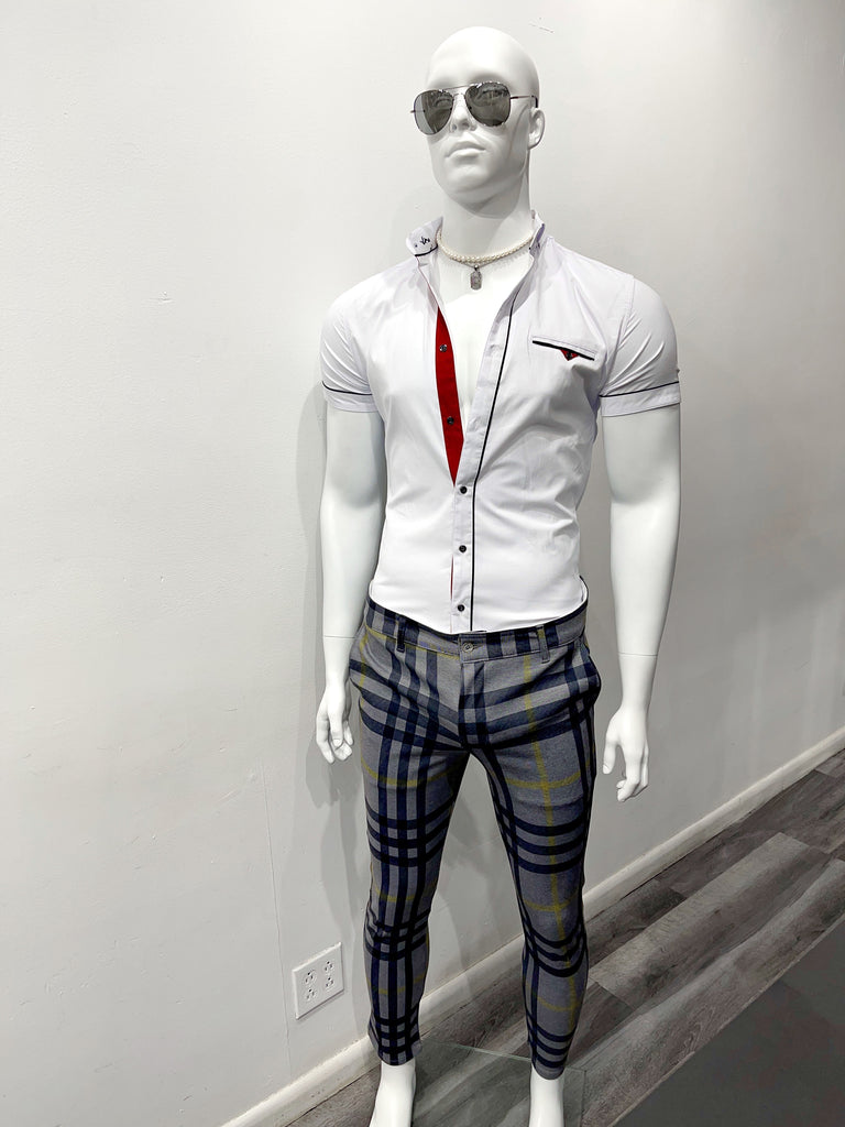 A white mannequin wearing mirrored sunglasses, a gold chain necklace with a pendant, a white, short-sleeved button-down shirt with red and blue details opened halfway down the front, and grey slim fit pants with a dark blue and yellow plaid pattern.