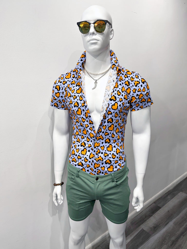 a mannequin dressed in sunglasses, a silver chain necklace with a silver shark tooth on it, a light blue shirt with orange leopard spots shaped like hearts, and 5-pocket spruce green shorts. The shirt is unbuttoned to his waist.
