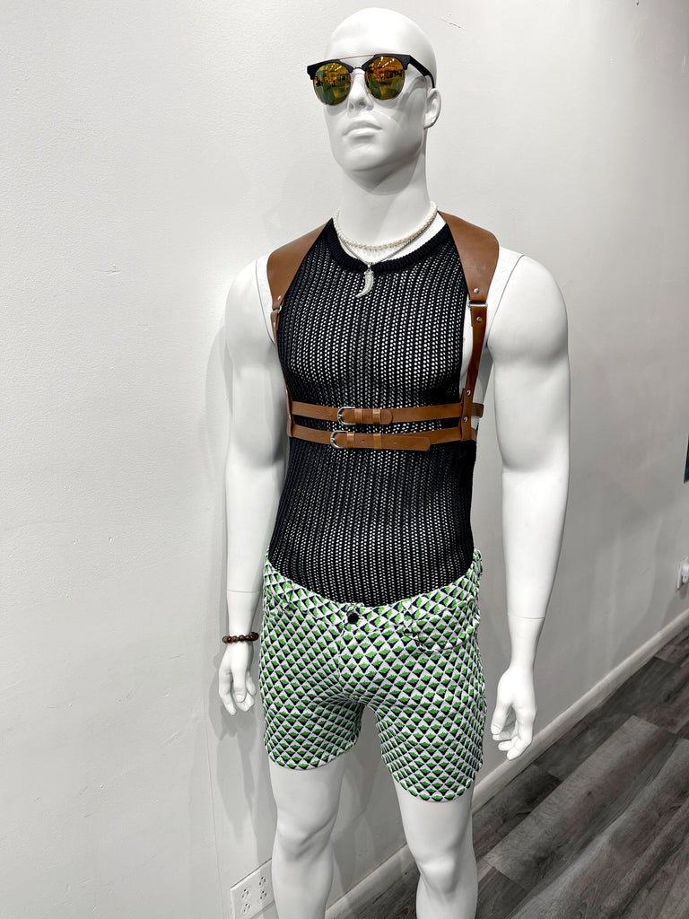 A white mannequin wearing colorful mirrored sunglasses, a silver choker necklace, a silver chain necklace with a shark tooth pendant, a black knit tank top, a brown leather waist harness, and white knit shorts with a green and blue arrowhead pattern.
