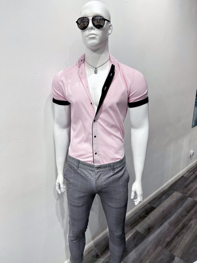 A mannequin wearing dark sunglasses, and a thin silver chain with a dog tag covered in fake diamonds, a pink button down short sleeved shirt, and grey plaid pants.
