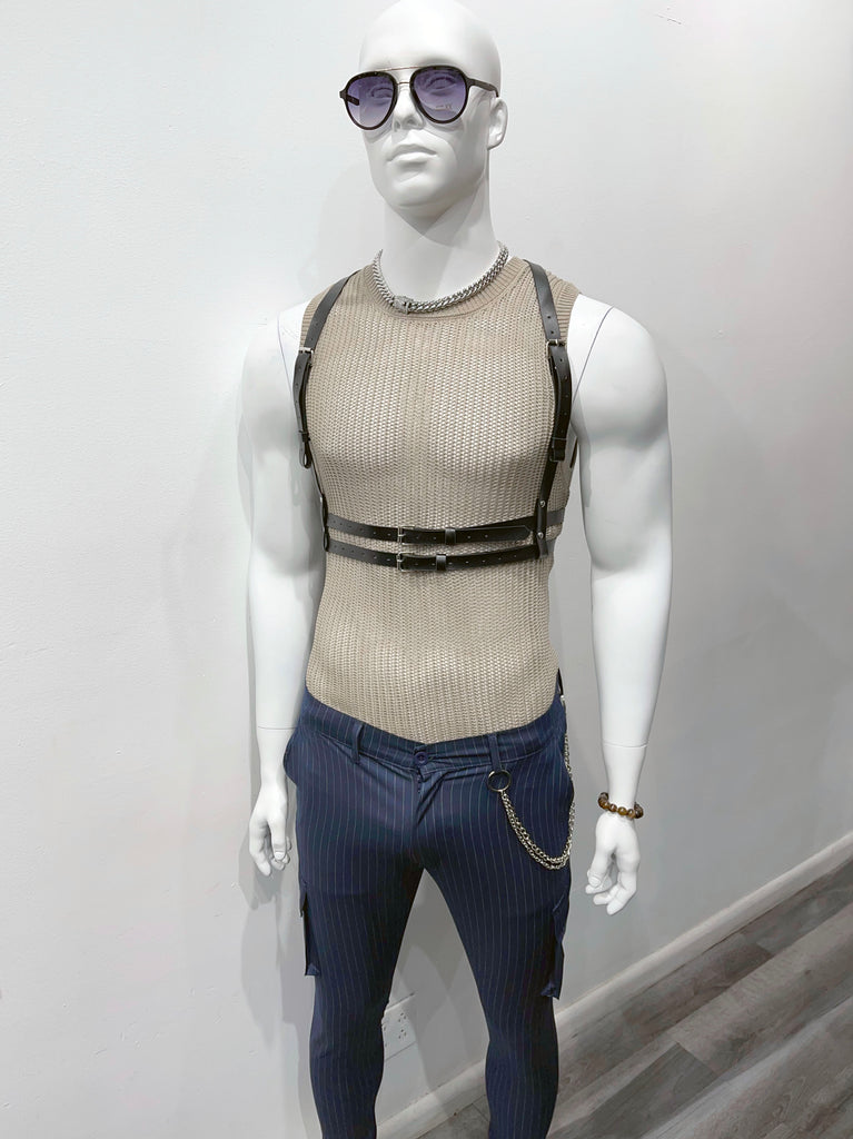 A mannequin wearing dark sunglasses, and a thick silver chain, a tan open knit tank top, a black waist harness, and navy utility pants with a fashion chain on the belt loop.