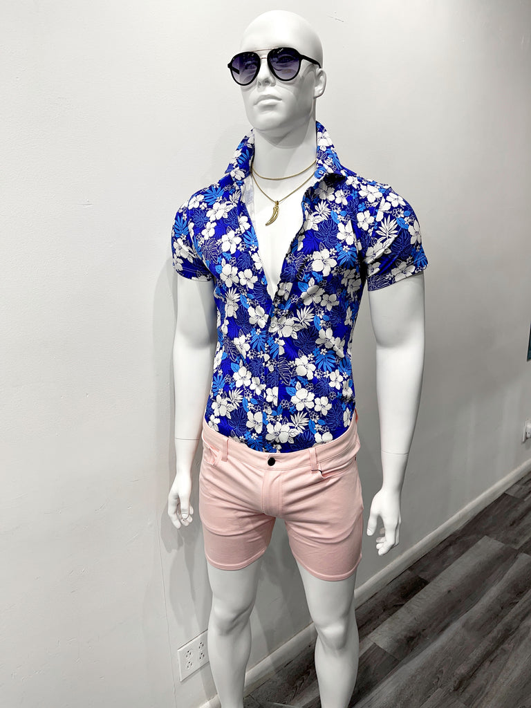 A white mannequin wearing dark gradient tint sunglasses, a silver necklace with a silver shark tooth charm on it, a short-sleeved button down blue and white floral shirt with the top four buttons opened, and pink 5-pocket stretch knit shorts.