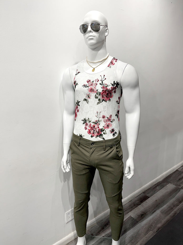 A white mannequin wearing dark, mirrored sunglasses, a gold choker necklace, a gold chain necklace with a gold pendant on it, a white mesh tank top with a red and green floral design, and green, slim fit fashion pants with utility pant design detailing.