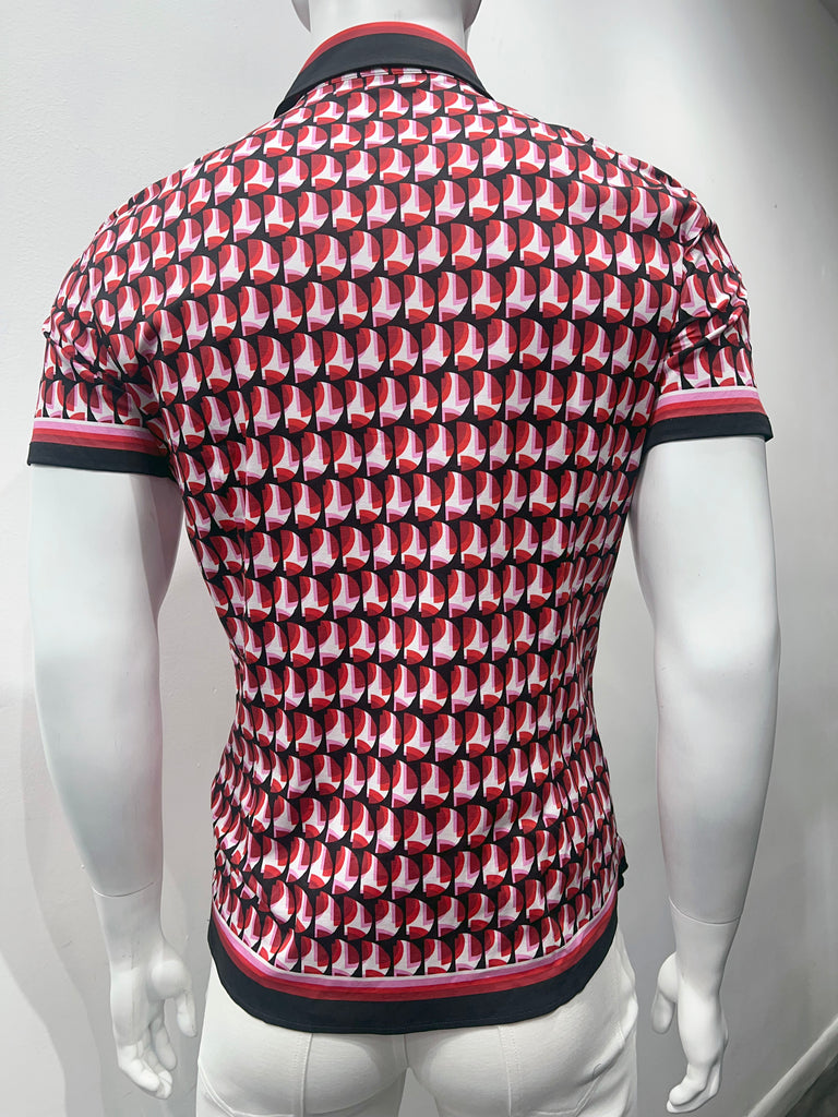 Short-sleeved button-down shirt as seen from the front. It has a colorful, mod pattern of layered red and pink half-circle slices as seen through a black stencil of half-circle cut-outs of the same size. The sleeve cuffs, collar and shirt hem have a thing stripe made up of smaller stripes of white, pink, red, dark red and navy-blue. 