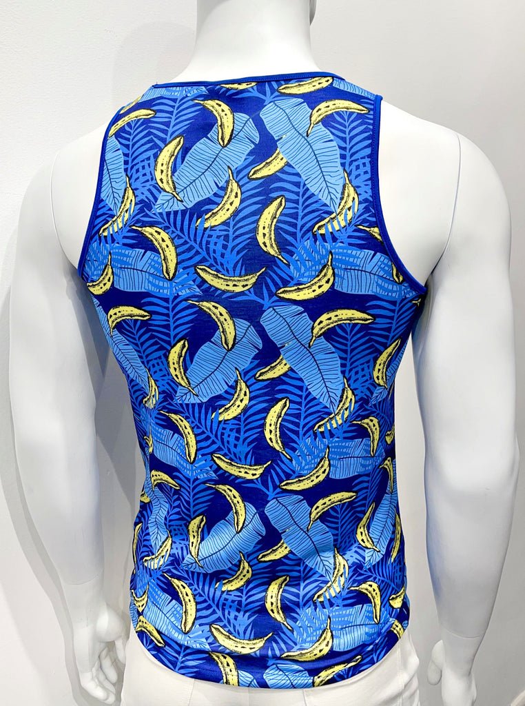  Tank top as seen from the back, with a colorful graphic print comprised of light blue leaves, royal blue ferns, and bananas, all on a navy blue background. There is royal blue piping on both sides of the shoulder straps.