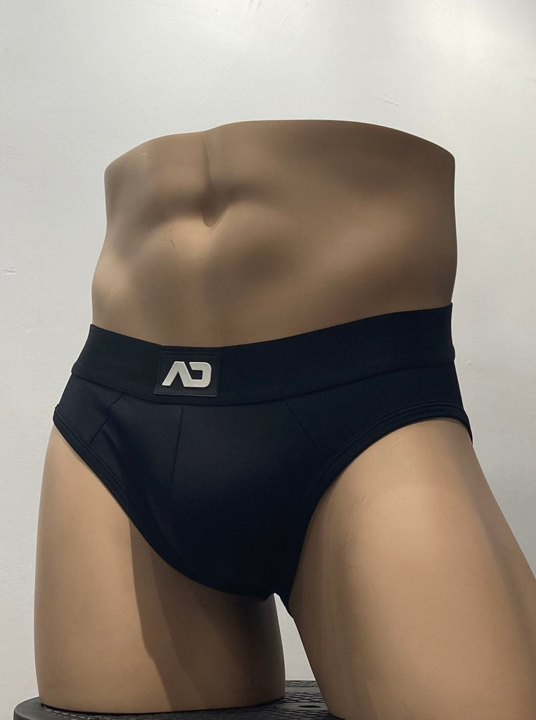 Black stretch brief, as seen from the front. It has a black waistband with a brand emblem on it, front and center.