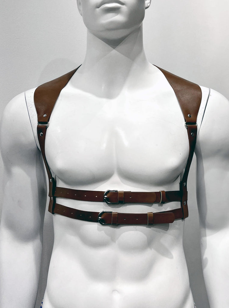 Brown harness as seen from the front. A single, thick shoulder strap goes over each shoulder, extending down the front of the torso on each side. The shoulder strap gets thinner as it extends down, contouring the outer curvature of the chest. Each shoulder strap reaches down on either side of the chest and wraps around two thin torso straps that encircle the mid-torso horizontally and buckle in the front.