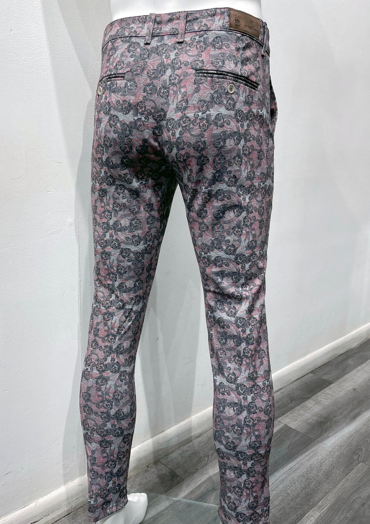 Flat front pants with a light blue, pink and grey layered ornate pattern, as seen from the back.