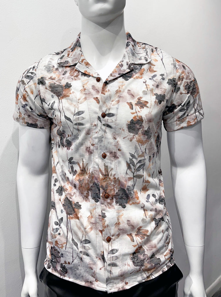 Short-sleeved, button-down off-white collared shirt, as seen from the front, with a floral pattern that looks like a water color painting comprised of different shades of dusty dark brown, tan, khaki green and grey. The buttons are brown.
