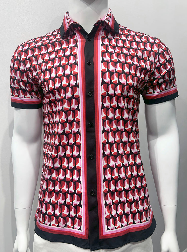 Short-sleeved button-down shirt as seen from the front. It has a colorful, mod pattern of layered red and pink half-circle slices as seen through a black stencil of half-circle cut-outs of the same size. The sleeve cuffs, collar and shirt hem have a thing stripe made up of smaller stripes of white, pink, red, dark red and navy-blue. The placket and buttons are navy-blue, so it looks like a dark navy-bue stripe down the center-front of the shirt.