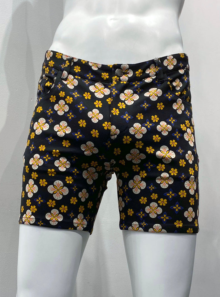 Zip-front, 5-pocket black stretch knit shorts as seen from the front, covered with a graphic floral pattern comprised of flowers with white petals, orange centers and pink accents, smaller orange flowers, and ever smaller orange and violet flowers.