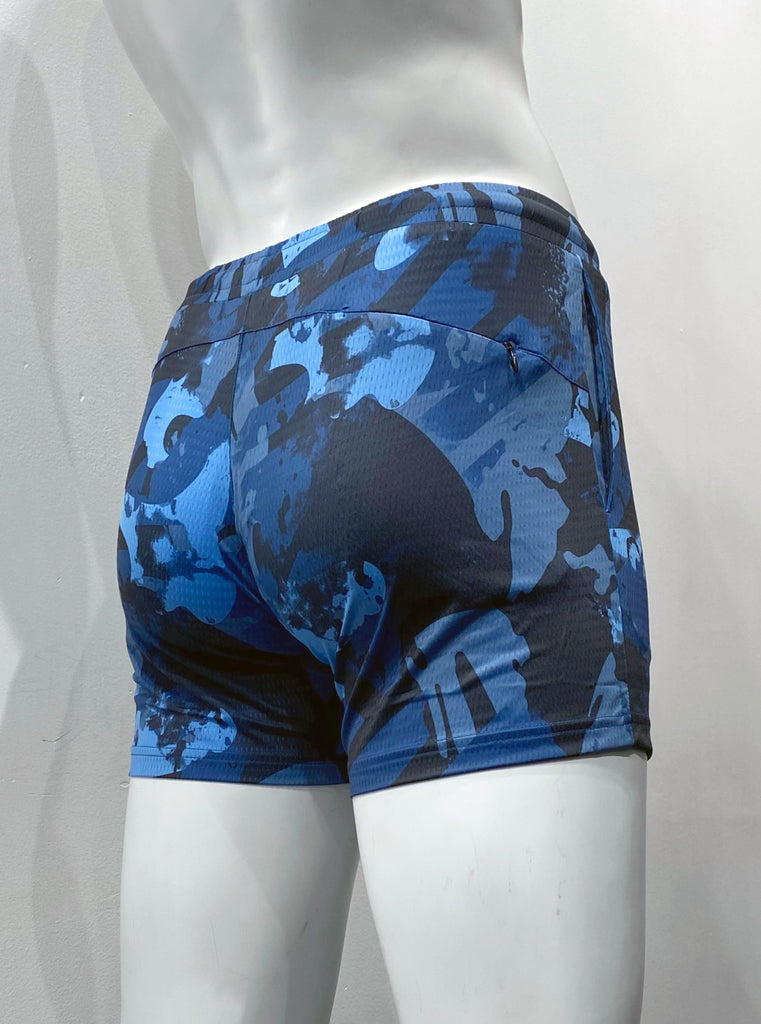 Slate blue, royal blue, light blue and black camouflage pattern athletic shorts with mesh fabric as seen from the back, with elastic waistband, body contouring seat seaming detail, and hidden zipper pocket on right back hip.