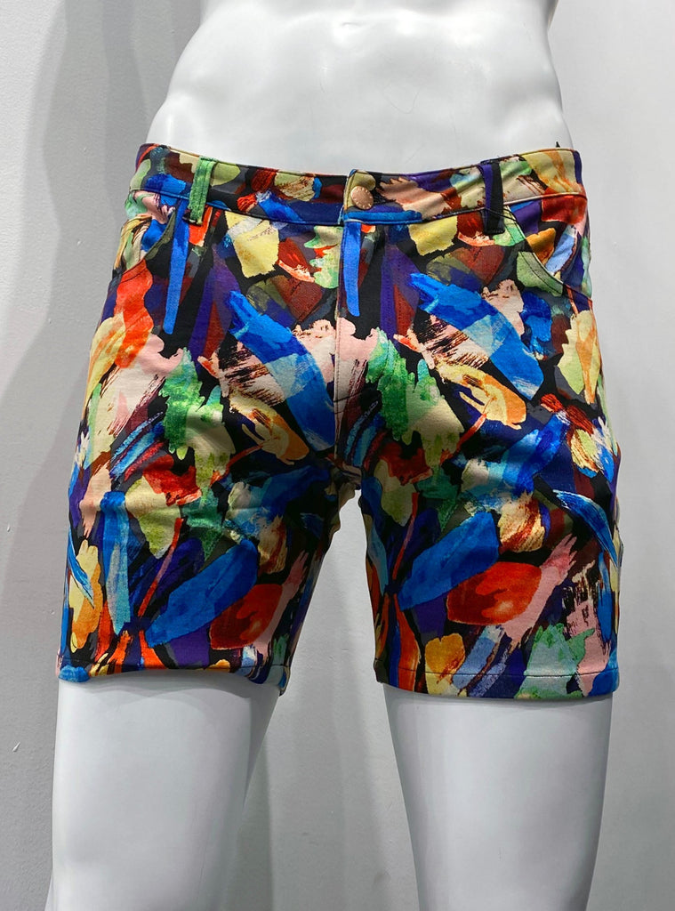 Zip-front, 5-pocket stretch knit shorts as seen from the front, covered with a vibrant pattern of rainbow-colored brush strokes that look like a water color painting.