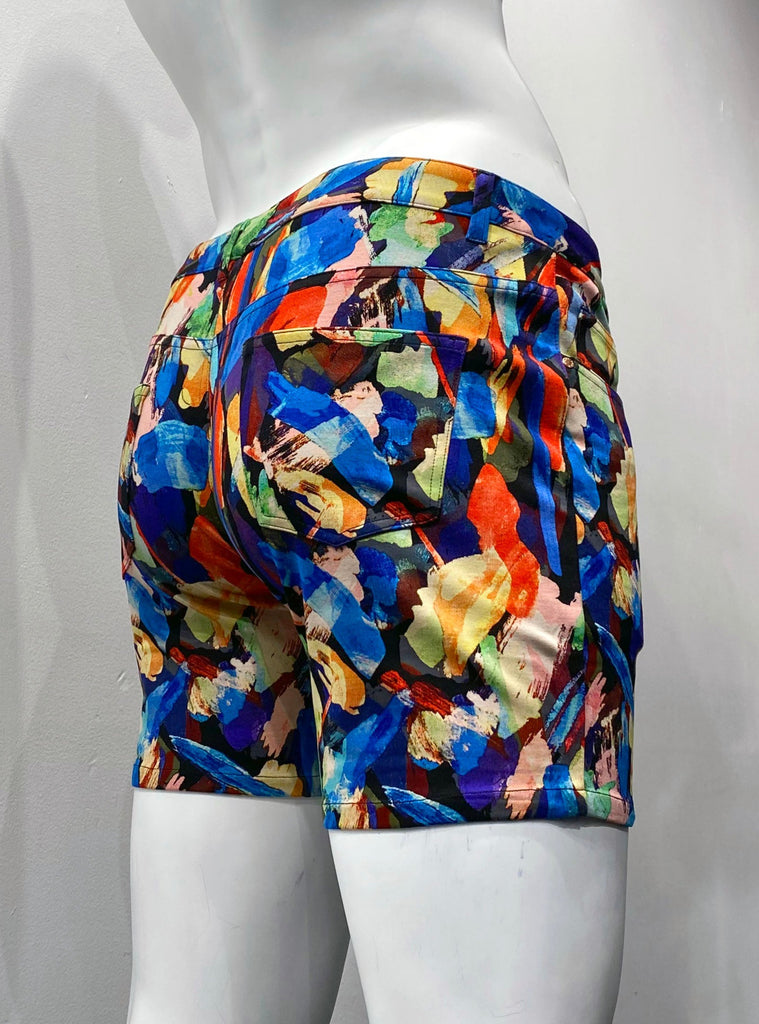 Zip-front, 5-pocket stretch knit shorts as seen from the back, covered with a vibrant pattern of rainbow-colored brush strokes that look like a water color painting.