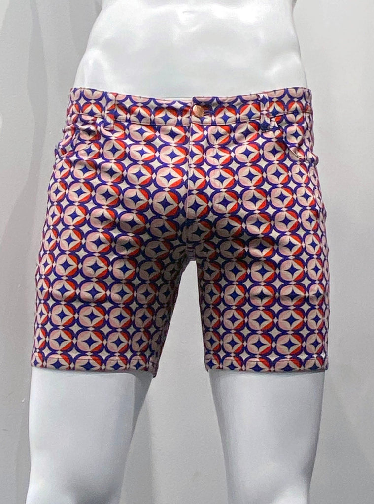 Zip-front, 5-pocket sienna pink stretch knit shorts as seen from the front, covered with a grid pattern of navy stars, each with 4 points, each encircled by 4 navy crescent shapes that make up the circle, with pink and red color blocking.