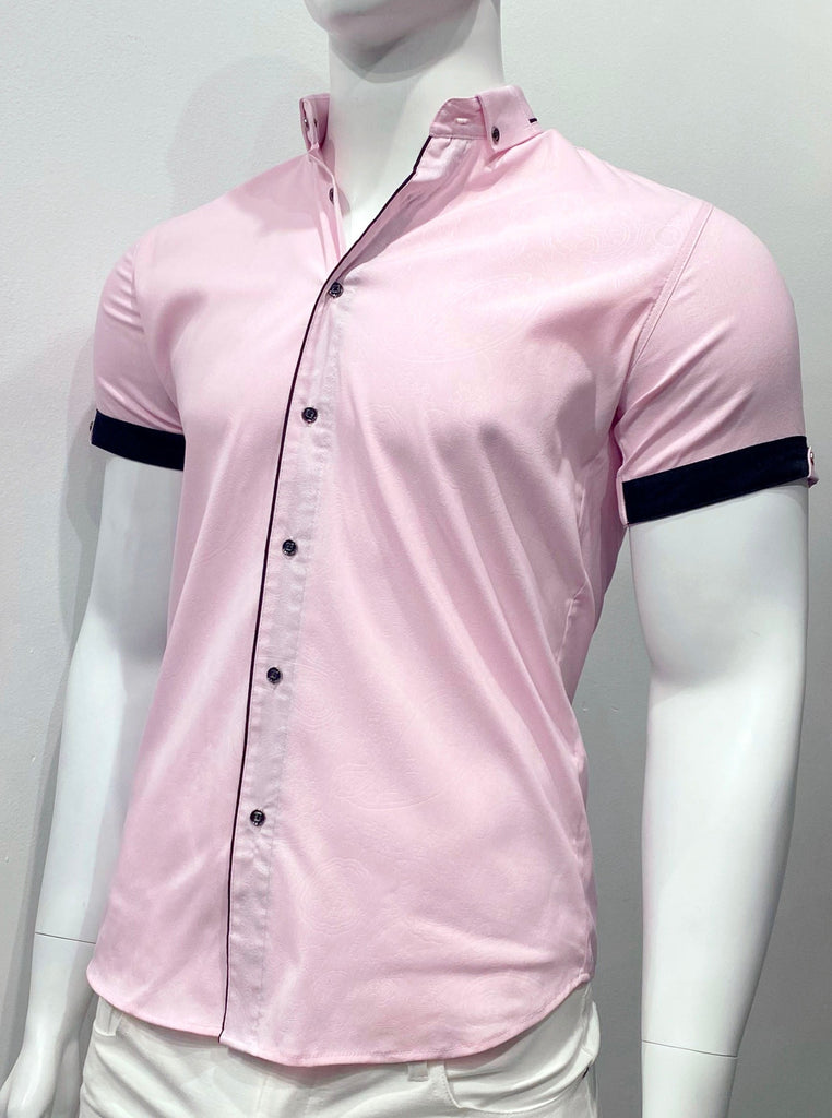 Pink short-sleeved button down shirt as seen from the front. The buttons are navy blue. The sleeve cuffs and the inside of the outer placket are navy blue. The edge of the outer placket is navy blue so it looks like navy blue piping that extends vertically up the front of the shirt, along the outer edge of the placket. There are navy blue collar buttons. There is a subtle paisley pattern woven into the pink fabric.