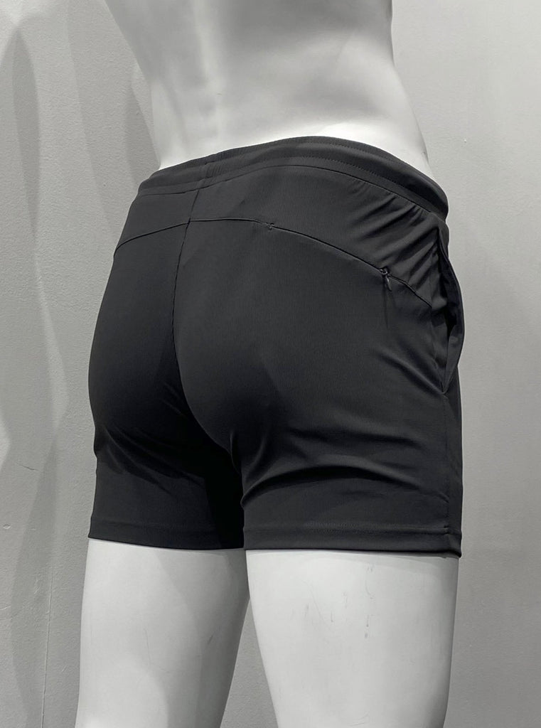Charcoal grey athletic shorts with lightly ribbed fabric as seen from the back, with elastic waistband, body contouring seat seaming detail, and hidden zipper pocket on right back hip.