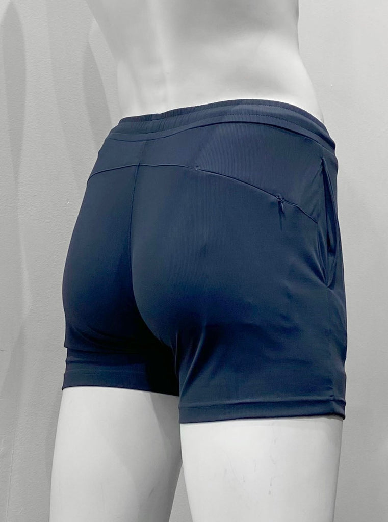 Navy blue athletic shorts with lightly ribbed fabric as seen from the back, with elastic waistband, body contouring seat seaming detail, and hidden zipper pocket on right back hip.