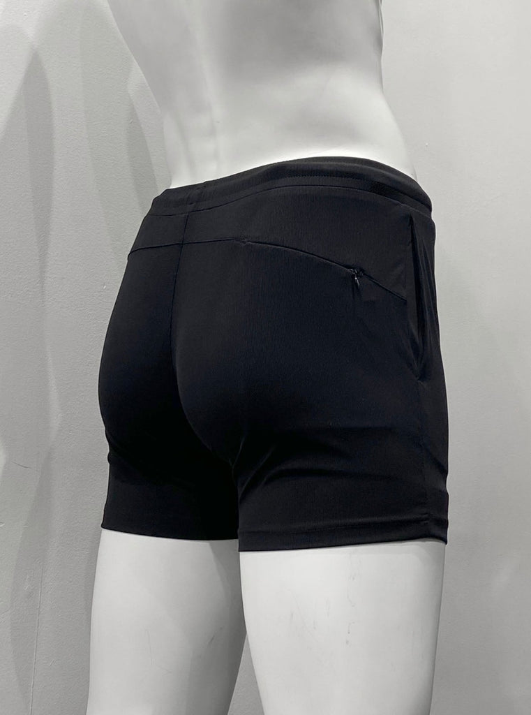 Black athletic shorts with lightly ribbed fabric as seen from the back, with elastic waistband, body contouring seat seaming detail, and hidden zipper pocket on right back hip.