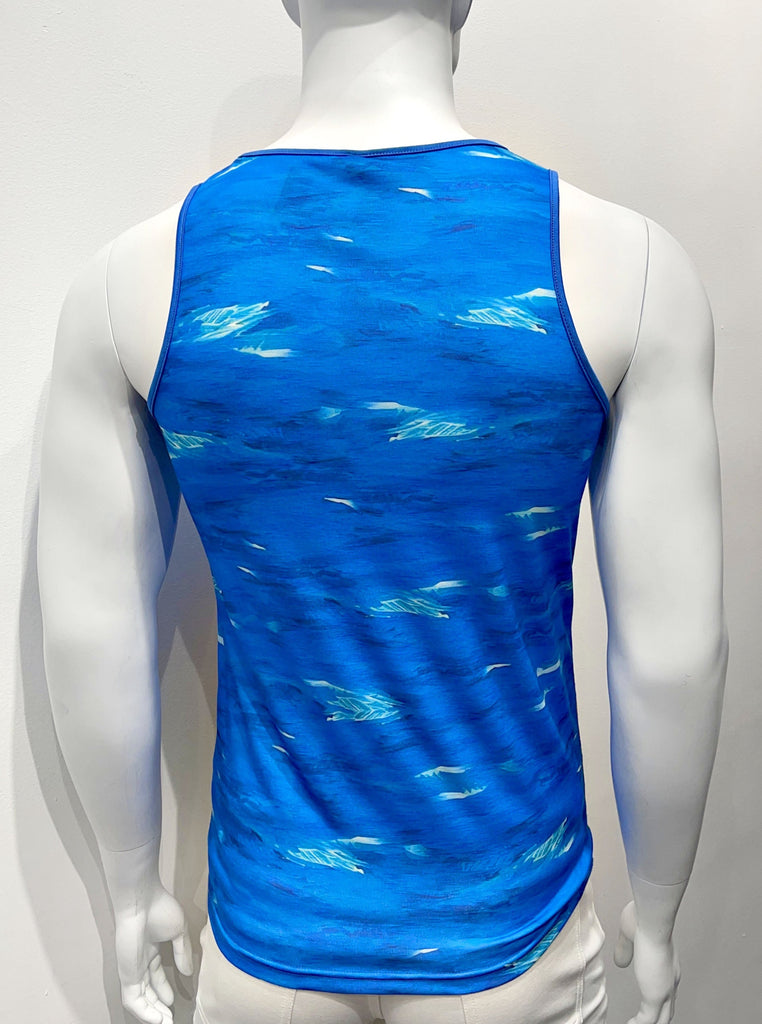 Tank top as seen from the back. It is covered with a colorful graphic print of royal blue water with bold, yellow and orange colored sunflowers along the bottom of the tank top. There is blue piping on both sides of the shoulder straps.