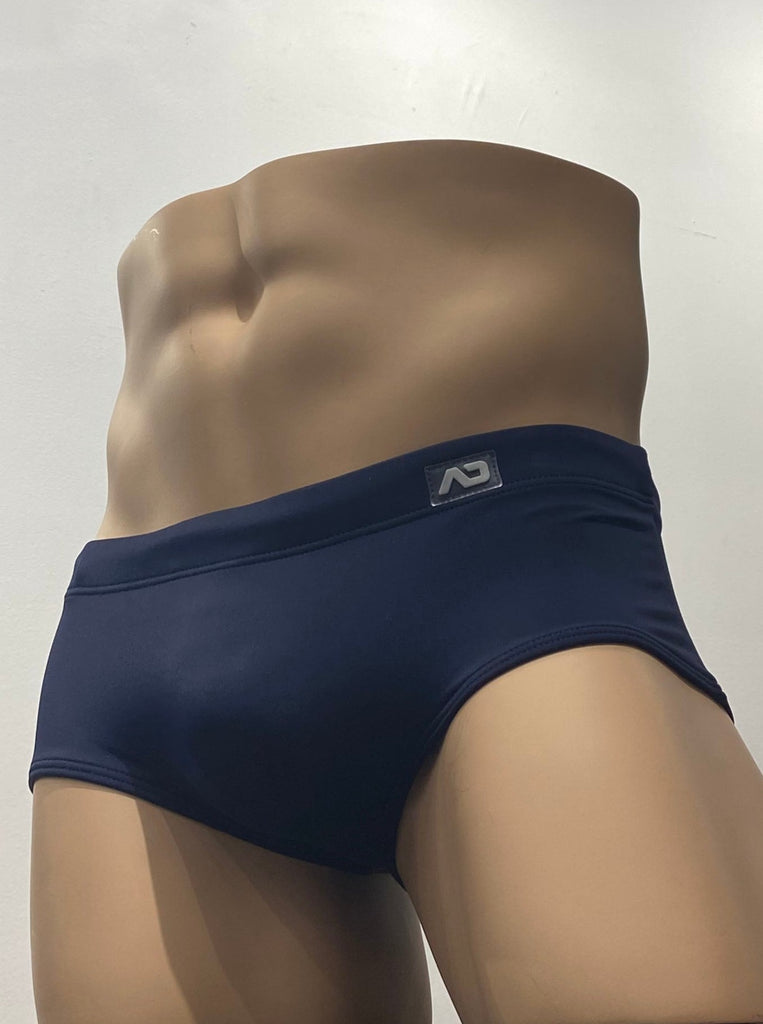  Navy blue sunga swim brief as seen from the front, with a brand emblem on the waistband above the left hip.