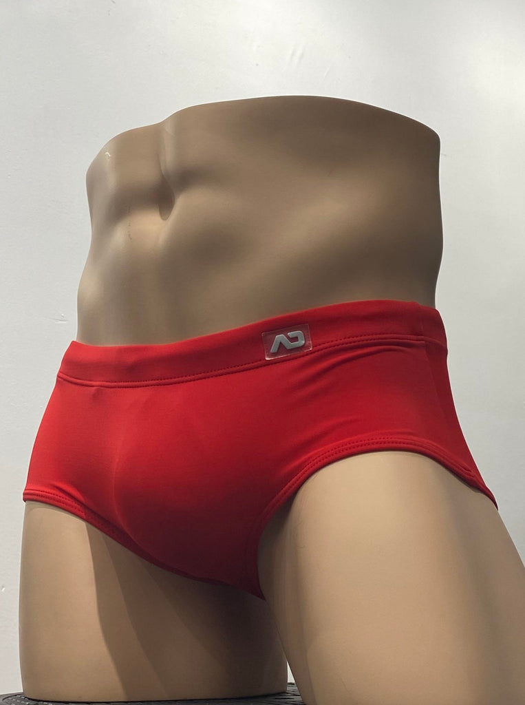 Red sunga swim brief as seen from the front, with a brand emblem on the waistband above the left hip.