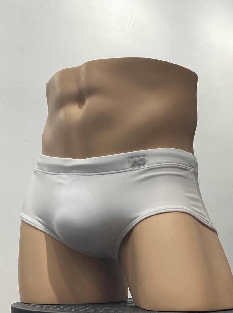 White sunga swim brief as seen from the front, with a brand emblem on the waistband above the left hip.
