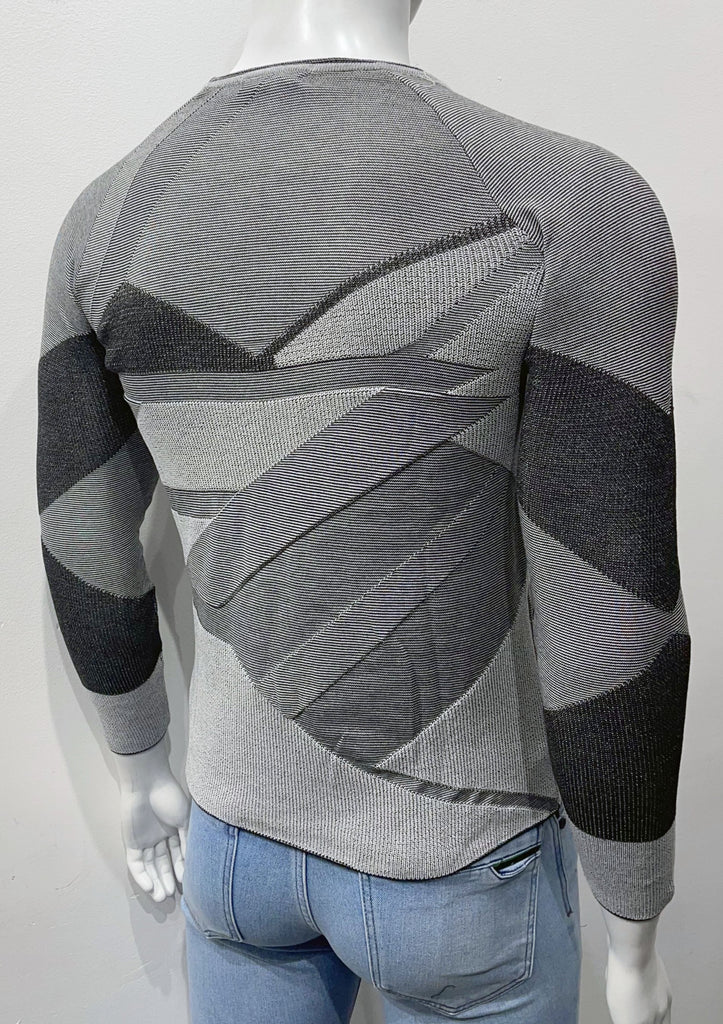 Slim fit crew neck sweater covered with an angular patchwork pattern of varying shades of black, grey, and ecru, as well as varying weave textures, as seen from the back.