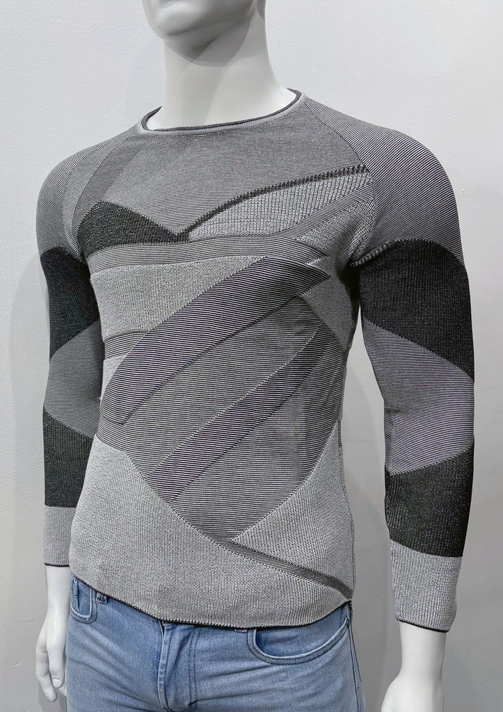 Slim fit crew neck sweater covered with an angular patchwork pattern of varying shades of black, grey, and ecru, as well as varying weave textures, as seen from the front.