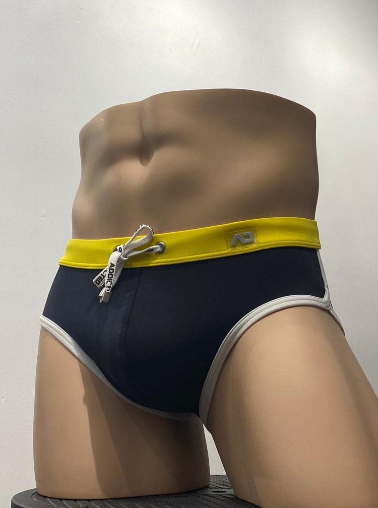 Black swim brief as seen from the front, with yellow waistband and white piping around the leg openings. The drawstring is white, has a brand logo pattern on it, and small silver metal aglets at the each end.